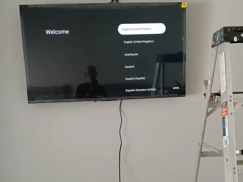 Televisión montada en la pared mostrando la pantalla de bienvenida, con el cable bajando recto a la toma